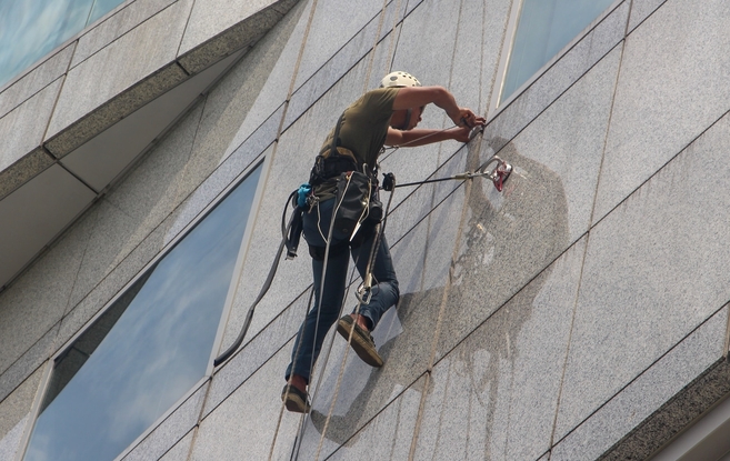 worker in harness suspended by lanyard outside of a tall building